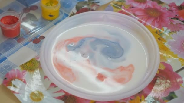 液体中の塗料の混合 子供の認知実験 ブラシからの塗料のドロップは白い液体に落ちます 色の違うガッシュを食べる 液体は白いプラスチック板に注がれます — ストック動画