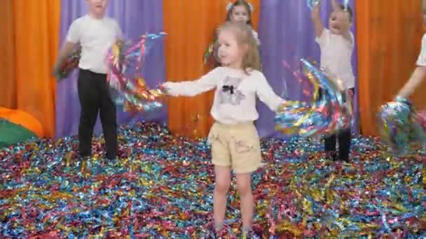 Colored ribbons fly in different directions. Bright childrens emotions. Children jump holding foil confetti in their hands. — Stock Video