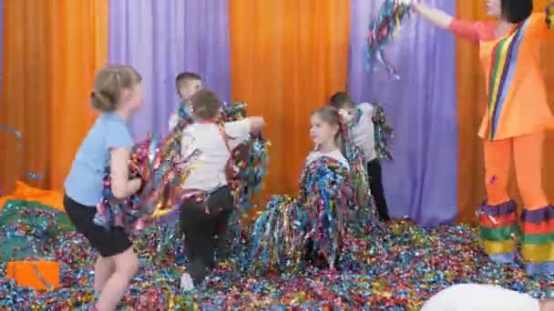 Farbige Bänder fliegen in verschiedene Richtungen. Helle Kindergefühle. Kinder springen mit Folienkonfetti in der Hand. Kinder frieren regungslos. — Stockvideo