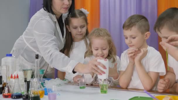 Chemische Experimente für Kinder. Frau gießt grüne Substanz in klares Glas. Die Kinder sind überrascht. Das Mädchen hält einen langen grünen Wurm in der Hand. Raum ist mit künstlichem Rauch gefüllt. — Stockvideo