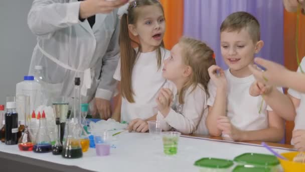 Chemische Experimente für Kinder. Frau gießt grüne Substanz in klares Glas. Die Kinder sind überrascht. Das Mädchen hält einen langen grünen Wurm in der Hand. Raum ist mit künstlichem Rauch gefüllt. — Stockvideo