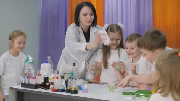 Chemical experiments for children. Woman pours a green substance into a clear glass. Children are surprised. The boy takes a long green worm out of the liquid. Room is filled with artificial smoke. — Stock Video