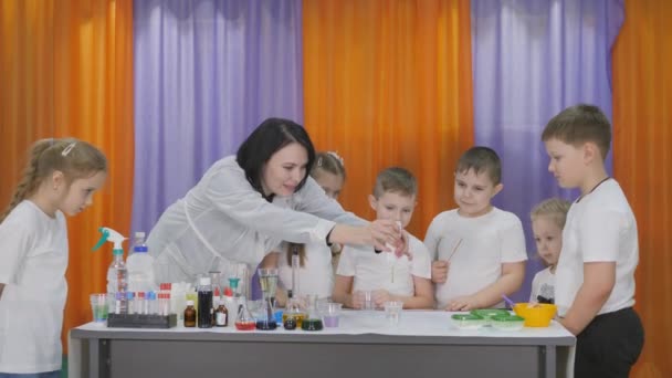 Esperimenti chimici per bambini. La donna versa una sostanza verde in un bicchiere trasparente. I bambini sono sorpresi. Il ragazzo tira fuori un lungo verme verde dal liquido. La stanza è piena di fumo artificiale . — Video Stock