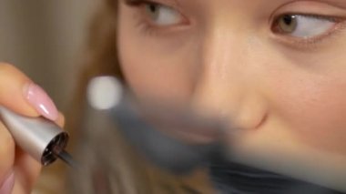 Makyaj yapıyorum. Genç kız aynaya bakar ve maskarasını sürterek gözlerinin kirpiklerine sürter..