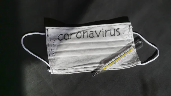 Koronavírus. Orvosi eldobható gézkötszerek vannak az asztalon. A higanyüveg hőmérője védőorvosi maszkon nyugszik.. — Stock Fotó