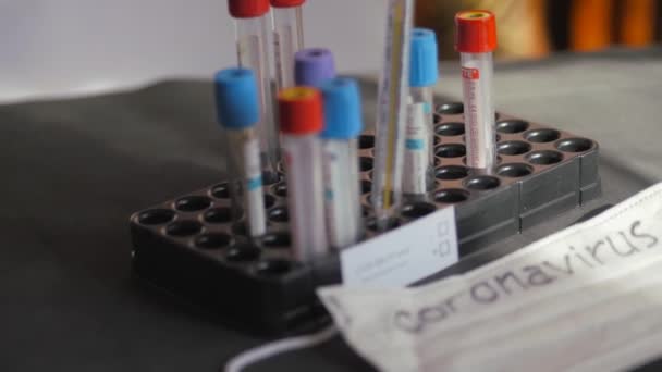 Coronavirus. Tıbbi test tüpleri organizatörde. Tıbbi tek kullanımlık sargı bezleri masanın üstünde. Bir cıva cam termometre koruyucu bir tıbbi maskenin üzerinde duruyor.. — Stok video