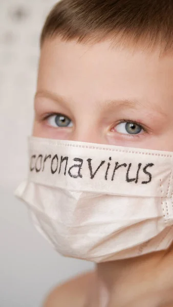 Medisch masker op het gezicht van de kinderen. Op het witte masker staat een zwart inscriptie Coronavirus. De blonde jongen is voorzichtig met het virus.. — Stockfoto