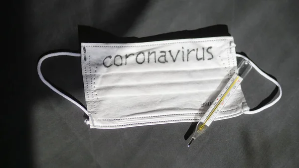 Coronavirus. Las vendas de gasa desechables médicas están sobre la mesa. Un termómetro de vidrio de mercurio descansa sobre una máscara médica protectora . —  Fotos de Stock