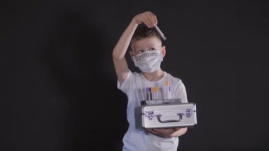 Çocuğun elinde metal bir bavul var. Çocuk, virüs için bir numuneyle tıbbi test tüpünü inceliyor. Çocuk virüse dikkat ediyor. Salgın Mart 2020. Coronavirus. COVID-19