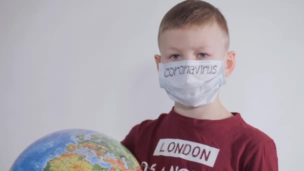 Junge hält einen Globus in der Hand, ein Modell des Planeten Erde. Kind hält ein Schild mit der Aufschrift: COVID-19. Junge ist vorsichtig mit dem Virus. Pandemie März 2020. Coronavirus. — Stockvideo