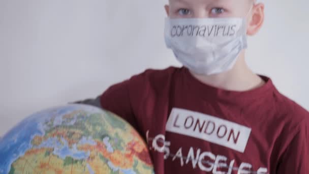 Jongen heeft een wereldbol, een model van de planeet Aarde. Kind draagt een bord met de inscriptie: GOD SAVE US. Jongen is voorzichtig met het virus. Pandemie maart 2020. Coronavirus. — Stockvideo