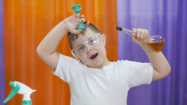 Çocuğun elinde renkli sıvı mataraları var. Yüzünde koruyucu şeffaf gözlüklü bir çocuk. Çocuklar için kimyasal deneyler. Çocuklar için eğlenceli deneyler. Çocuklar eğlenir ve öğrenir. Parlak