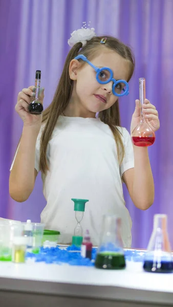 子供は色のついた液体のフラスコを持っている。顔に青い丸メガネの可愛い女の子。子供のための化学実験。子供のための楽しい実験。子供たちは楽しく学びます。明るい子供たち — ストック写真