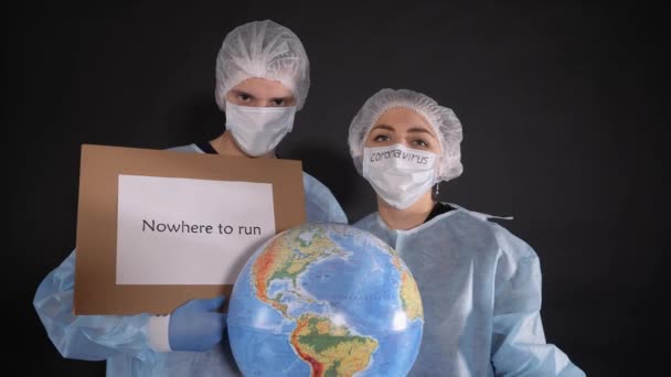 保護服を着た男と女はどこにも逃げず助けてという言葉で看板を掲げています。少女は地球、地球のモデルを保持しています。人々の顔に保護マスク。白いマスクの上に — ストック動画