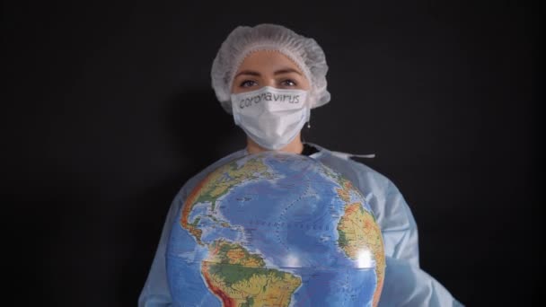 Woman in protective clothing holds a sign that reads covid-19. The girl is holding a model of the earth, a globe. — Stock Video