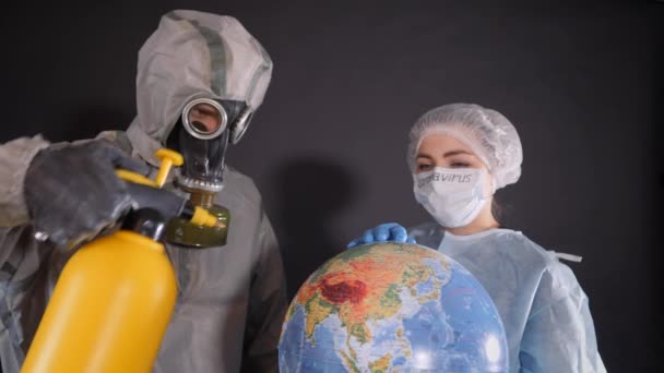 Ontsmetting van de planeet Aarde. Man in een chemisch beschermingspak en een gasmasker. Guy houdt een gele spuitbus vast. Jonge vrouw in beschermende kleding. Op de voorkant van een beschermend medisch masker — Stockvideo