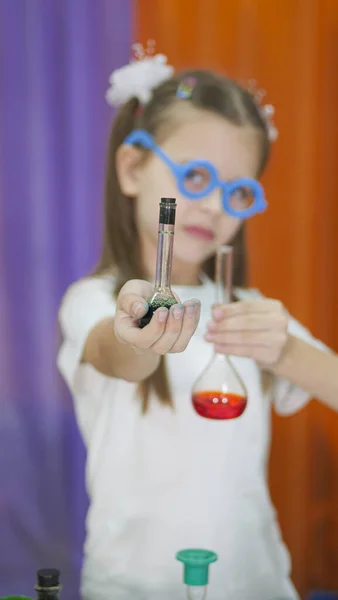 子供は色のついた液体のフラスコを持っている。顔に青い丸メガネの可愛い女の子。子供のための化学実験。子供のための楽しい実験。子供たちは楽しく学びます。明るい子供たち — ストック写真