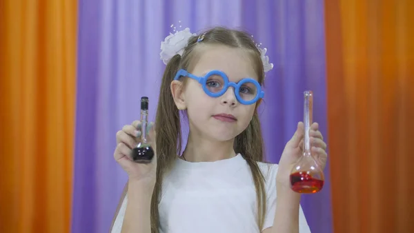 El niño sostiene frascos de líquido de color. Linda chica con gafas redondas azules en su cara. Experimentos químicos para niños. Divertidos experimentos para niños. Los niños se divierten y aprenden. Niños brillantes — Foto de Stock