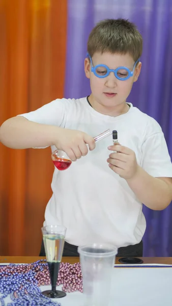 Мальчик в синих круглых очках на лице. Ребенок держит фляжки с цветной жидкостью. Химические эксперименты для детей. Веселые эксперименты для детей. Дети веселятся и учатся. Яркие дети — стоковое фото