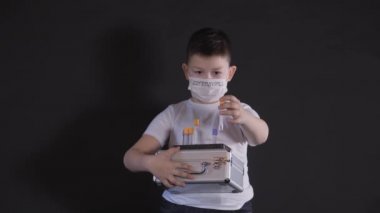 Çocuğun elinde metal bir bavul var. Çocuk, virüs için bir numuneyle tıbbi test tüpünü inceliyor. Çocuk virüse dikkat ediyor. Salgın Mart 2020. Coronavirus. COVID-19