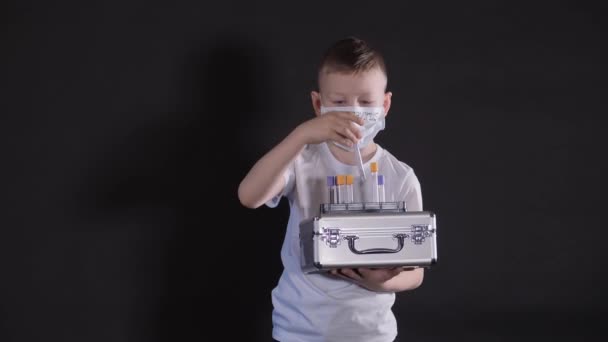 De jongen houdt een metalen koffer vast. Kind onderzoekt een medische reageerbuis met een monster voor het virus. Jongen is voorzichtig met het virus. Pandemie maart 2020. Coronavirus. COVID-19 — Stockvideo
