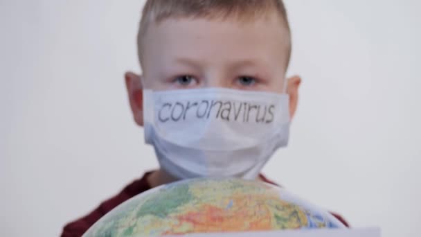 Jongen heeft een wereldbol, een model van de planeet Aarde. Kind draagt een bord met de inscriptie: COVID-19. Jongen is voorzichtig met het virus. Pandemie maart 2020. Coronavirus. — Stockvideo
