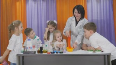Çocuklar için kimyasal deneyler. Öğretmen sarı bir kasede elastik karışımı karıştırır. Oda yapay dumanla dolu..