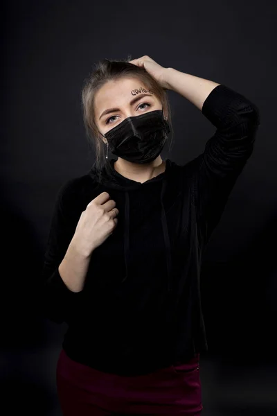 Femme dans un masque de protection noir avec les mots covid-19 écrit sur son front . Photo De Stock