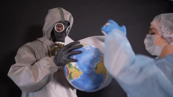 Man in a chemical protection suit and a gas mask. The guy is holding a model of the Earth, a globe. young woman in protective clothing. On the face of a protective medical mask. Treatment of the — Stock Video