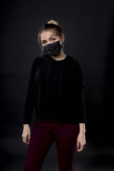 Woman in a black protective mask with the words covid-19 written on her forehead. — Stock Photo, Image