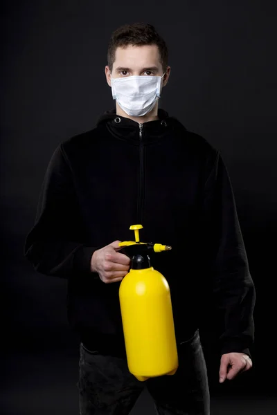 Un uomo con una pistola gialla in mano. Sul viso di un giovane uomo, una maschera medica copre il naso e la bocca. Protezione antivirale . — Foto Stock