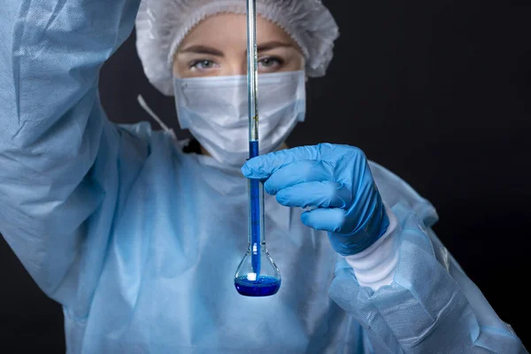 A drop of blue liquid falls into a transparent vessel from a glass tube of a heat-resistant water-measuring water-indicating device. Young woman in protective clothing. On the face of a protective