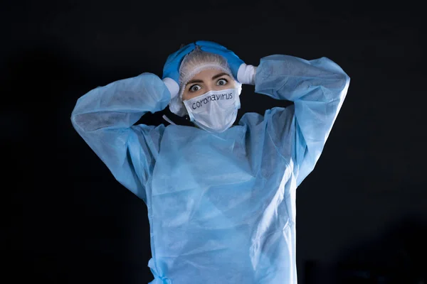 Young woman in protective clothing. On the face of a protective medical mask with the inscription coronavirus. The girl holds her head with both hands.