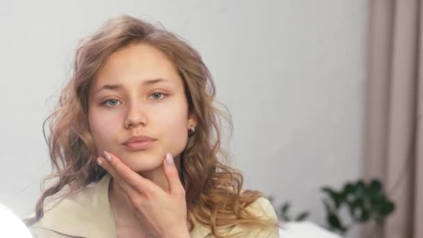 Chica se mira en el espejo y endereza su cabello. Chica traza el contorno de su cara y pómulos con su mano . — Vídeos de Stock