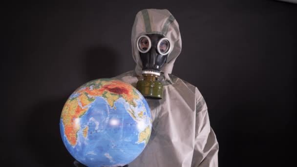 化学防護服の男とガスマスクだ 男は地球 地球のモデルを保持している 惑星地球の汚染 次の銘文を持つプラカードが世界に添付されています Covid — ストック動画
