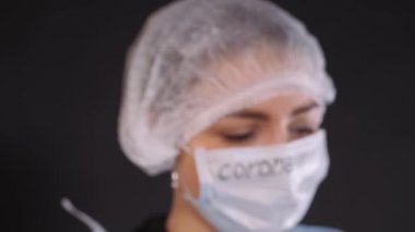 Test tüpleri doktorun ellerinde çapraz. Kız bir deney tüpünü biyomateryalle inceliyor. Koruyucu giysili genç bir kadın. Koruyucu bir tıbbi maskenin yüzünde. Elleri mavi lateks eldiven giymiş. Beyaz maskeli