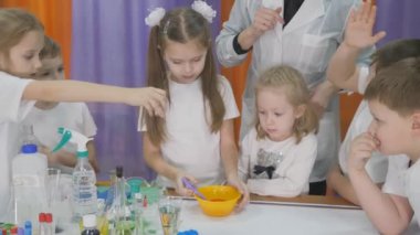 Çocuklar için kimyasal deneyler. Sarı bir kaseye malzemeler ekle ve karıştır. Çocuklar için eğlenceli deneyler. Bir kadın bilişsel bilim dersleri veriyor. Çocuklar için eğlenceli oyunlar. Oda yapay dumanla dolu..
