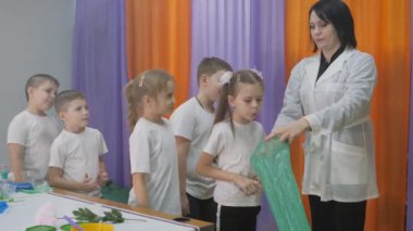 Çocuklar için kimyasal deneyler. Çocuklar için eğlenceli deneyler. Bir kadın bilişsel bilim dersleri veriyor. Çocuklar akciğer hacmini ölçer Kız uzun yeşil bir torbaya üflüyor ve şişiriyor. Çocuklar eğlenir ve öğrenir. Parlak çocukların duyguları..