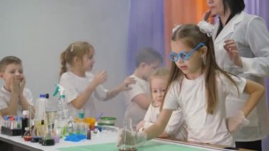 Çocuklar için kimyasal deneyler. Kız şeffaf bir tabağı malzemelerle sarkıtıyor. Çocukların parlak duyguları. Çocuklar için eğlenceli deneyler. Bir kadın bilişsel bilim dersleri veriyor. Çocuklar için eğlenceli oyunlar. Oda yapay dumanla dolu..