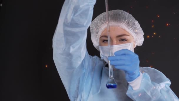 Una gota de líquido azul cae en un recipiente transparente de un tubo de vidrio de un dispositivo de medición de agua resistente al calor. Las chispas vuelan alrededor de la persona . — Vídeos de Stock