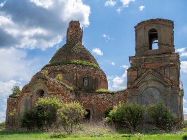 Beyaz bulutlu mavi gökyüzüne karşı Ortodoks Kilisesi 'nin kalıntıları. Duvarlar, yeşil çalılıklardaki kırmızı tuğlalar..