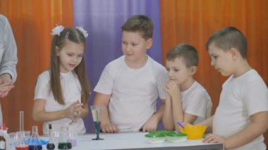 Çocuklar için kimyasal deneyler. Çocuklar için eğlenceli deneyler. Kadın berrak bir bardağa mavi bir sıvıyla ilaç ekliyor. Sıvının içinde mavi kabarcıklar yükseliyor. Oda yapay dumanla dolu..