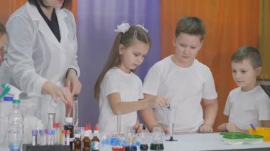 Çocuklar için kimyasal deneyler. Çocuklar için eğlenceli deneyler. Kız bir bardak suya mavi boya ekler ve çözeltiyi karıştırır. Oda yapay dumanla dolu..