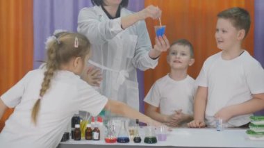Çocuklar için kimyasal deneyler. Çocuklar için eğlenceli deneyler. Çocuk şeffaf bir plastik bardaktan masaya mavi kar döker. Oda yapay dumanla dolu..