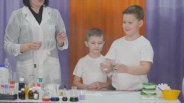 Çocuklar için kimyasal deneyler. Çocuklar için eğlenceli deneyler. Kadın elleriyle sihirli hareketler yapıyor ve mavi sıvı çocukların şaşkınlığı için buza dönüşüyor. Oda yapay dumanla dolu..