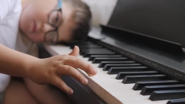 电子钢琴指按钢琴键 音乐课 孩子在课上累坏了 躺在乐器的钥匙上 这个男孩懒洋洋地从事音乐 皮带落在乐器上 那孩子害怕了 — 图库视频影像