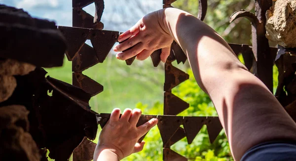 Hands reach for the metal bars in the window. Outside the window, the landscape was beautiful. Hands hold a metal rod. The old walls of red brick. Windows of an ancient temple, in the wall of red brick. The hole in the wall is sealed with metal bars