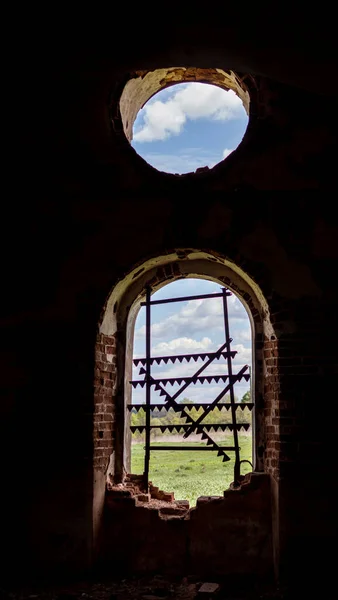 Windows of an ancient temple, in the wall of red brick, in the form of an arch. The hole in the wall is sealed with metal bars with teeth. A view of the world through the bars. Rose window in the wall of a ruined old Orthodox Church.
