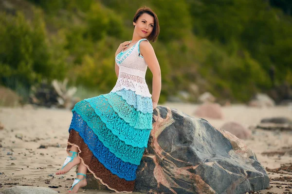 Brunette in the knit sundress handmade sitting on a rock by the sea