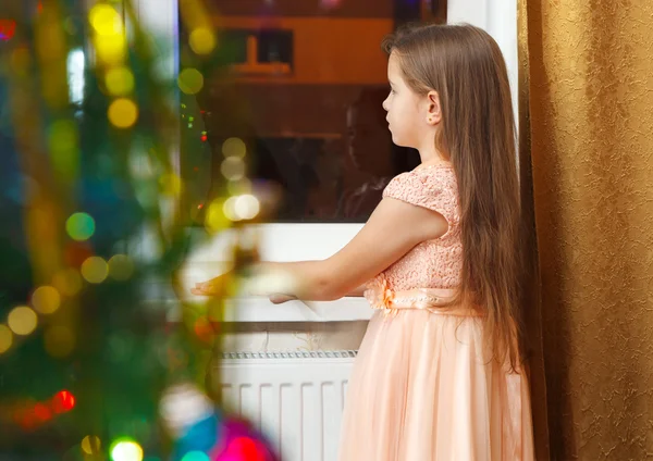 Küçük kız Noel'de pencerenin önünde ayakta — Stok fotoğraf